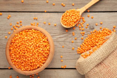 Tahta kaşıkta kırmızı mercimek ve gri ahşap arka planda çanta. Kapat..