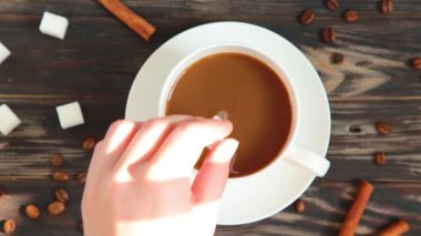 Bir kadın bir fincan aromatik kahvenin içinde şeker karıştırır. Bir fincan aromatik kahve ahşap bir masaya konur..