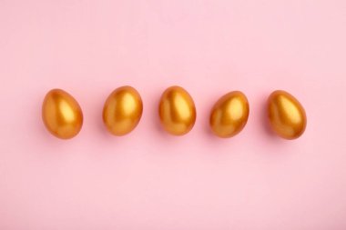 Pembe pastel arka planda altın yumurtalar. Üst görünüm.