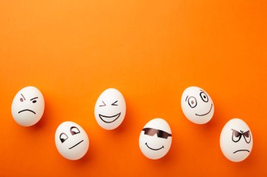 Turuncu arka planda farklı duyguları olan komik Paskalya yumurtaları. Paskalya kompozisyonu. Üst görünüm