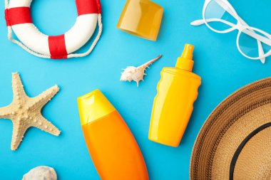 Mavi arka planda şapka, gözlük ve diğer aksesuarlarla güneş kremi şişesi. Güneş yanığı için kozmetik. Güneş koruma kremi