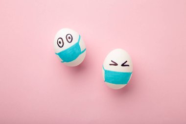Beyaz Paskalya yumurtaları pembe arka planda koruyucu tıbbi maske takıyor. Karantina konseptinde paskalya. VIRUS COVID-19 'u durdurun. Uzayı kopyala Maskeli yumurta. Üst görünüm