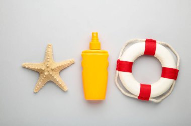 Gri arka planda plaj aksesuarları olan güneş koruma şişesi. Üst görünüm.