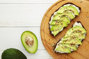 Avokado sandviçi. Beyaz arka planda taze kesilmiş avokadolarla yapılan koyu çavdar ekmeği. Üst görünüm