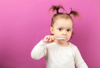 Pembe arka planda dişlerini fırçalayan tatlı bir kız. Üst görünüm