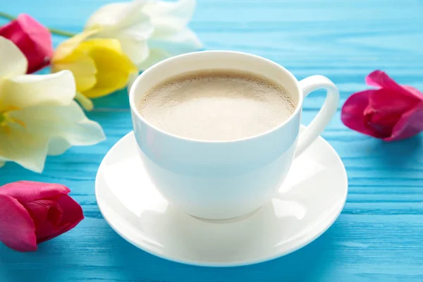 Cup of coffee with tulips on blue background. Top view