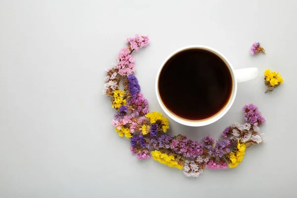 Cup of coffee with flowers on grey background. Flat lay, top view