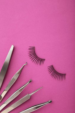 Pembe arka planda cımbızlı takma kirpik seti. Minimalizm. Üst görünüm