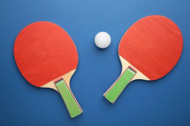 Masa tenisi raketleri ve top mavi arka planda. Üst görünüm