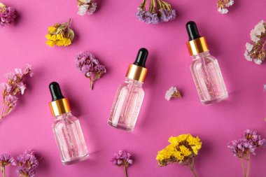 Güzellik kozmetik cilt yağı şişede. Mor arka planda çiçekli ürünler. Üst Manzara. Metin için alanı kopyala