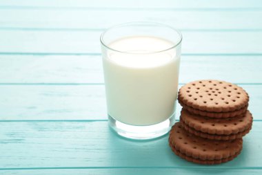 Çikolata parçalı kurabiye ve mavi ahşap arka planda bir bardak süt..