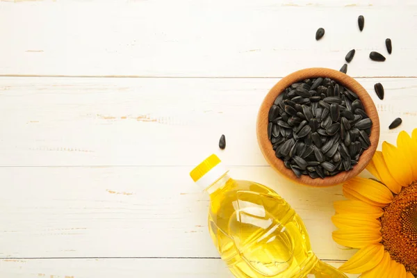 Sunflower oil, seed and sunflower on white wooden background. Top view