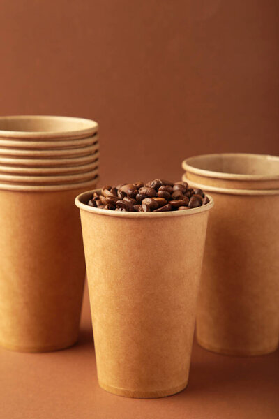 Coffee beans and paper coffee cup on brown background. Top view.