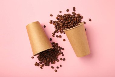 Kahve çekirdekleri ve pembe arka planda kağıt kahve fincanları. Üst görünüm.