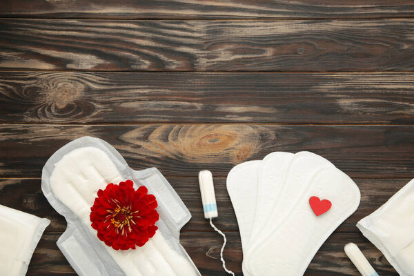 Менструальные тампоны и подушечки на коричневом фоне. Розовый цветок лежит на менструальной подушке. Менструационный цикл. Гигиена и защита. Вид сверху. Вертикальное фото