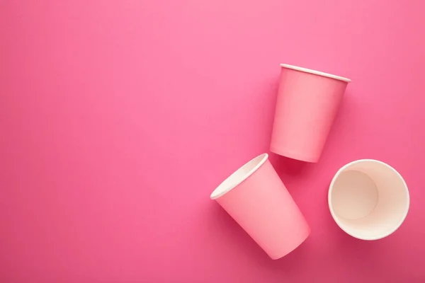 Disposable paper cups on a pink background.