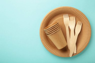 Eko kağıt sofra takımı. Kâğıt bardaklar, tabaklar, çantalar, fast food kapları ve mavi arka planda ahşap çatal bıçak takımı. Sıfır kayıp. Geri dönüşüm konsepti. Boşluğu kopyala