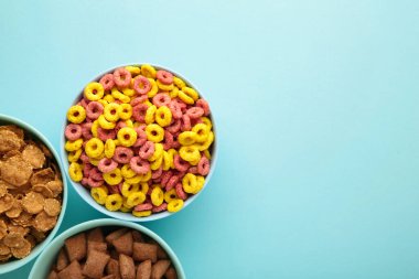 Mavi kaselerde çeşitli mısır gevrekleri, mavi arka planda hızlı kahvaltı. Üst görünüm