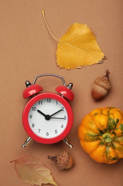 Kırmızı çalar saat, meşe palamudu ve kahverengi arka planda sonbahar yaprakları. Gün ışığından tasarruf zamanı sona erdi. Üst görünüm
