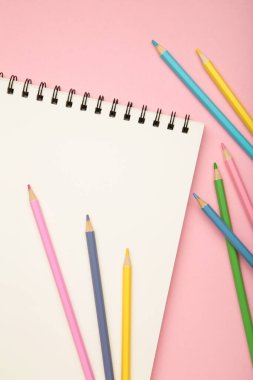 Sketchbook and colored pencils on pink background. Top view