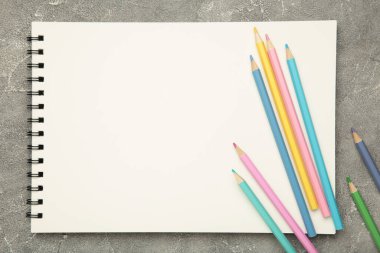 Sketchbook and colored pencils on grey concrete background. Top view