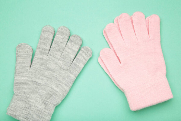 Grey and pink knitted gloves on mint background. Space for text