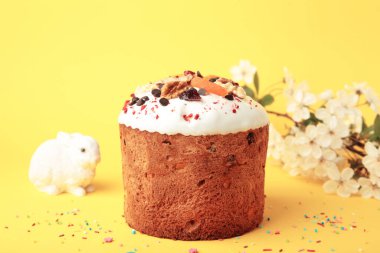 Geleneksel paskalya pastaları, rengarenk serpiştirilmiş yumurta, tavşan heykeli ve sarı arka planda bahar çiçekleri.