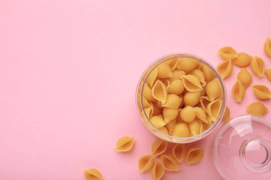 Conchiglie rigate. Pembe arka planda kavanozda çiğ çizgili kabuklu makarna. Metin için boşluk