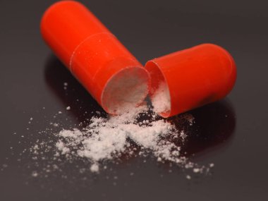 Beyaz ilaç ilacı içeren turuncu kapsülün yakın plan görüntüsü.