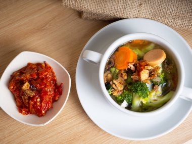 Sosis, brokoli, havuç içeren sebze çorbası beyaz bir porselen kasede küçük bir kase kırmızı biber ezmesi.