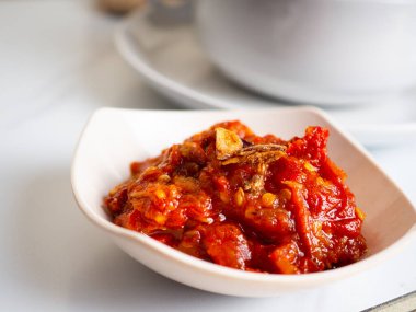 Sosis, brokoli, havuç içeren sebze çorbası beyaz bir porselen kasede küçük bir kase kırmızı biber ezmesi.