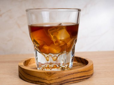 Ahşap bir masanın üzerinde bir fincan buzlu kahve ve bir kavanoz kabı. Karanlık ruh hali tarzında ateş et.