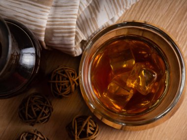 Ahşap bir masanın üzerinde bir fincan buzlu kahve ve bir kavanoz kabı. Karanlık ruh hali tarzında ateş et.