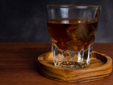 Ahşap bir masanın üzerinde bir fincan buzlu kahve ve bir kavanoz kabı. Karanlık ruh hali tarzında ateş et.