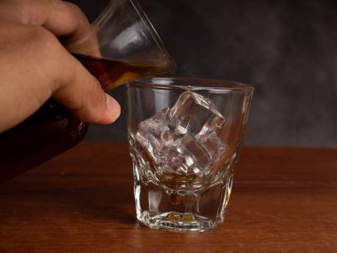 Ahşap bir masanın üzerinde bir fincan buzlu kahve ve bir kavanoz kabı. Karanlık ruh hali tarzında ateş et.