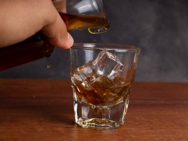 Ahşap bir masanın üzerinde bir fincan buzlu kahve ve bir kavanoz kabı. Karanlık ruh hali tarzında ateş et.