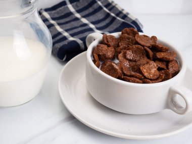 Beyaz bir mermer masaya konmuş beyaz bir kâse üzerinde süt bulunan mısır gevreği.