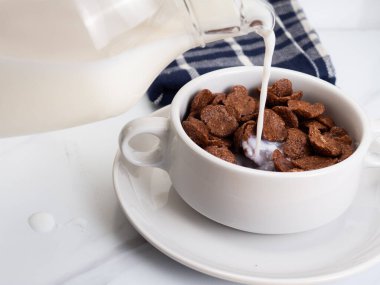 Beyaz bir mermer masaya konmuş beyaz bir kâse üzerinde süt bulunan mısır gevreği.