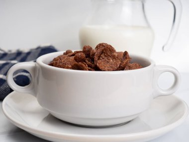 Beyaz bir mermer masaya konmuş beyaz bir kâse üzerinde süt bulunan mısır gevreği.