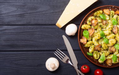 Ahşap arka planda fesleğen, peynir ve mantarlı ev yapımı patates gnocchi.