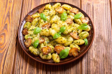 Ahşap arka planda fesleğen, peynir ve mantarlı ev yapımı patates gnocchi.