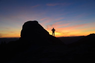 Dağ ve insan silueti parlak sabah arkaplanına karşı.
