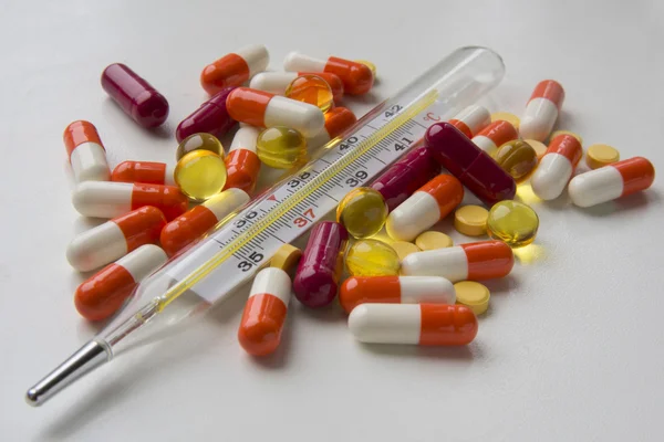 Pills and thermometer on white surface — Stock Photo, Image