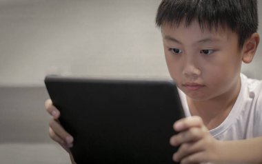Evde dijital tabletle oyun oynayan Asyalı çocuk dijital musluk ya da akıllı telefondan çizgi film izleyen çocuklar