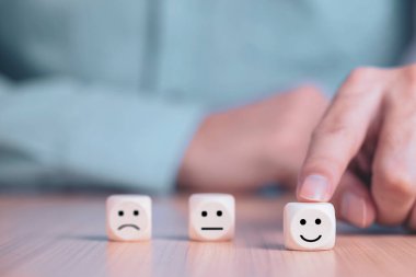 İş adamı bir gülümseme simgesi seçti: Ahşap blok, Hizmetler ve Müşteri memnuniyeti anketi konseptinde mutlu simgelerle karşı karşıya