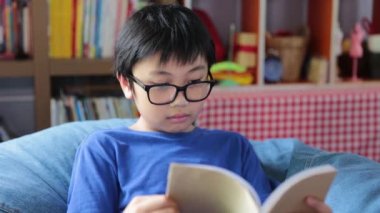 10-13 yıllık gözlüklü, gülümseyen Asyalı çocuk oturma odasındaki kanepede kitap okumayı seviyor. eğitim kavramı