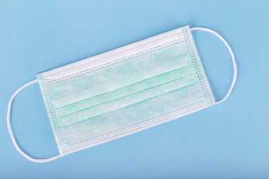 Korona virüsünü korumak için tıbbi maske. Mavi arka planda ağız ve burnu kaplayan lastik kulak bantları var.