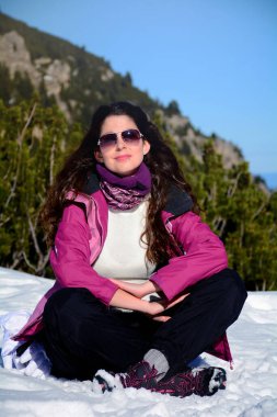 Kış dağında oturan kadın Kış güneşinin ve manzaranın tadını çıkarıyor 