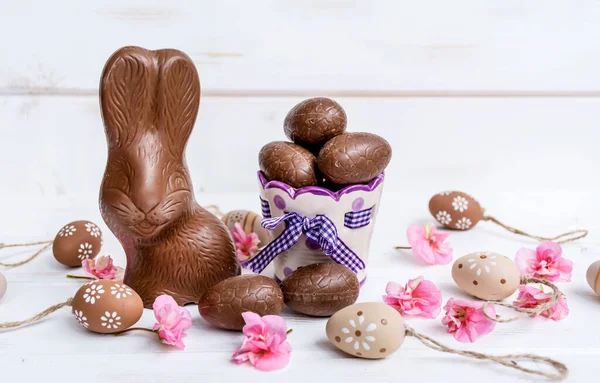 Chocolate Easter Bunny,Chocolate Eggs and Pink Flowers on a White Wooden Background .Easter Greeting Card