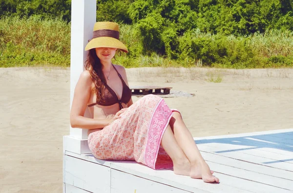 ストローハットの若い女性がビーチの桟橋に座っている — ストック写真